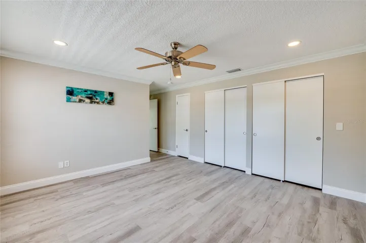 An expansive look at the primary bedroom showcasing a wall of extensive closet space, elegant crown molding, and recessed lighting.