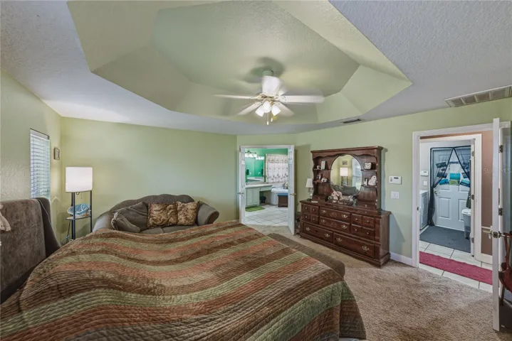 The primary bedroom has a tray ceiling with ceiling fan with light. The double door to the primary bathroom is in the background.