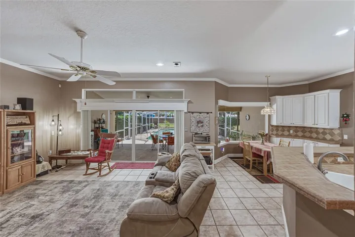 The great room has crown molding, ceramic tile flooring, ceiling fan and a four panel sliding door.