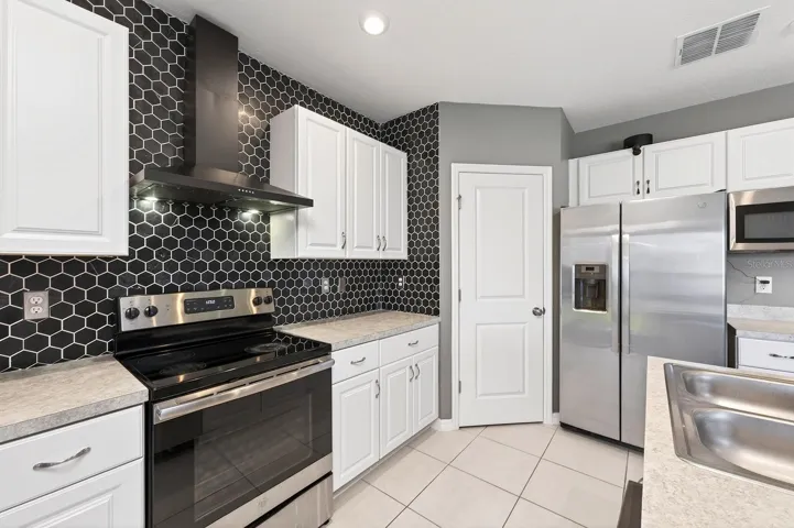 The STYLISH KITCHEN overlooks the main living areas and is thoughtfully designed with white cabinetry, a MODERN STONE BACKSPLASH (2023), stainless steel appliances, a sleek range hood, a Kitchen island with breakfast bar seating, and a walk-in pantry closet.