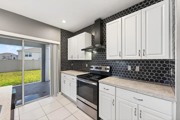 The STYLISH KITCHEN overlooks the main living areas and is thoughtfully designed with white cabinetry, a MODERN STONE BACKSPLASH (2023), stainless steel appliances, a sleek range hood, a Kitchen island with breakfast bar seating, and a walk-in pantry closet.
