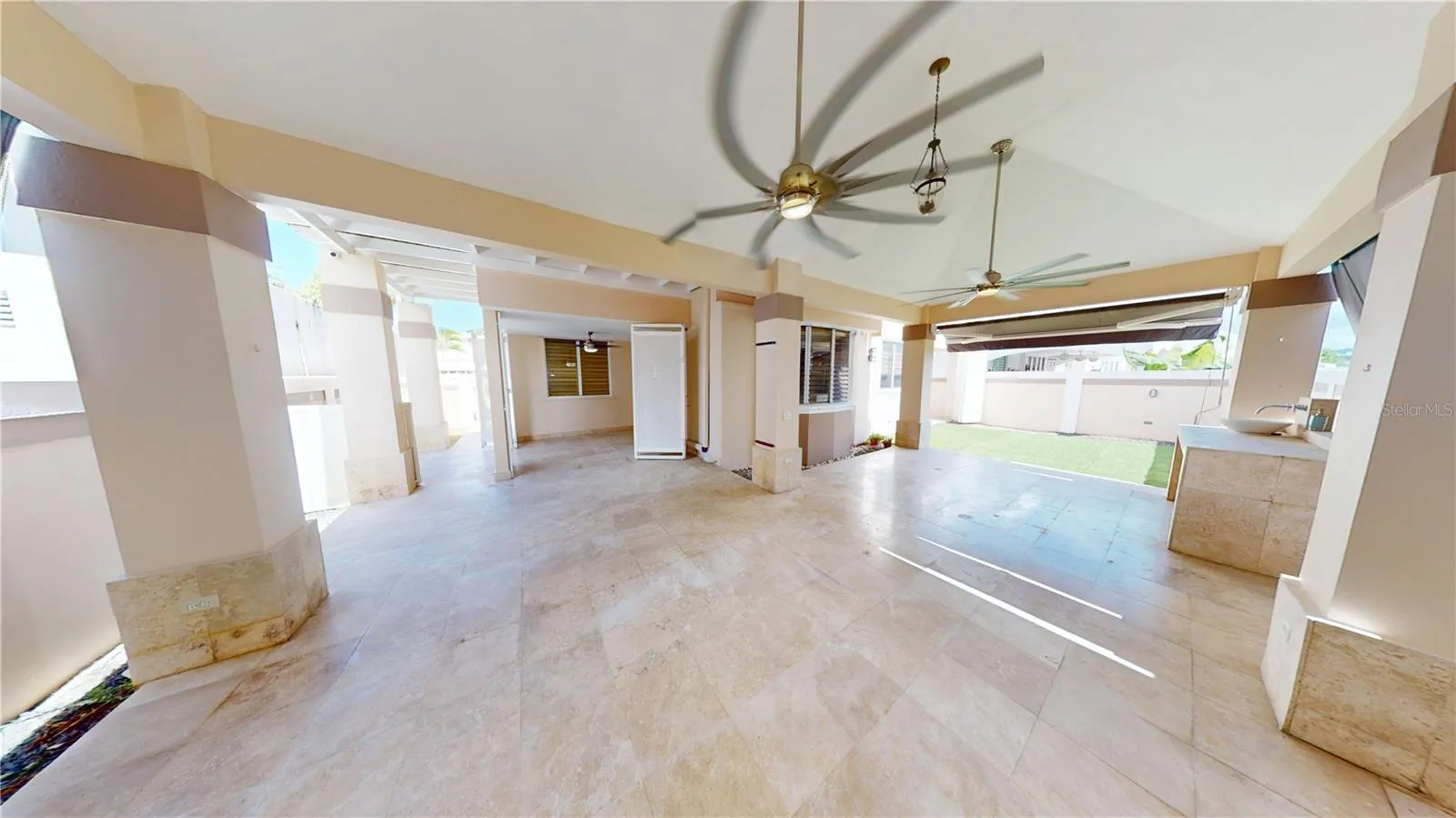 Spacious covered L-shaped terrace featuring high ceilings, a bar area and curtains.