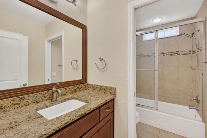 GUEST BATH WITH GRANITE COUNTERTOPS, FRAMED MIROR, POCKET DOOR THAT LEADS TO THE TOILET AND GLASS ENCLOSURE ON THE TUB/SHOWER.