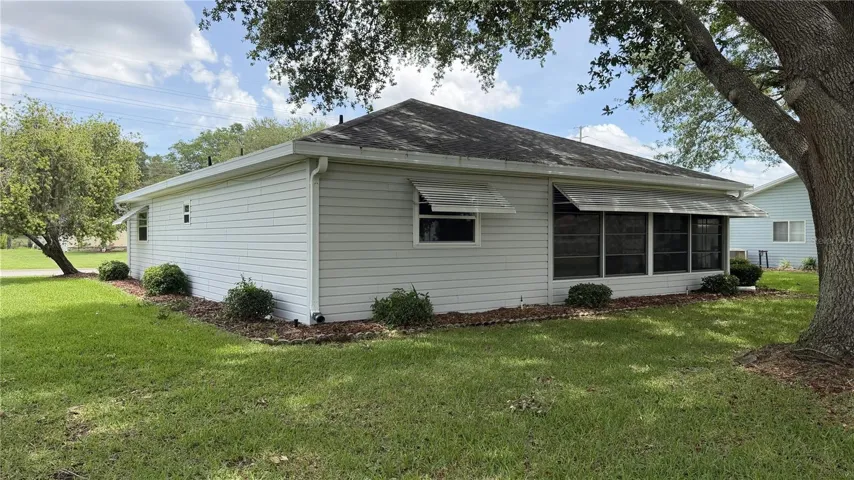 Side exterior with enclosed lanai, mature shade tree, and lawn