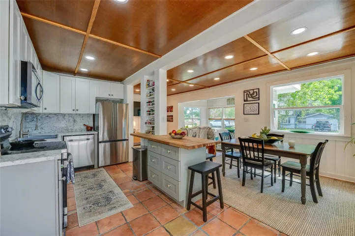 Kitchen and dining suite boasting high-end stainless steel appliances, a center island with a butcher block countertop, and marble-patterned backsplashes. The adjacent dining area sits beneath a large picture window overlooking the lush yard.