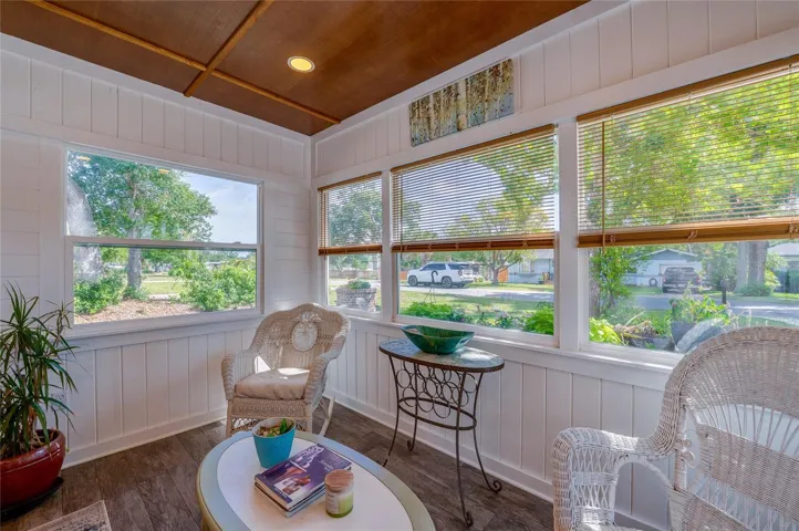 Sun-drenched enclosed porch featuring bright white paneling and large windows with views of the neighborhood. The space is beautifully anchored by a warm wood-paneled ceiling.