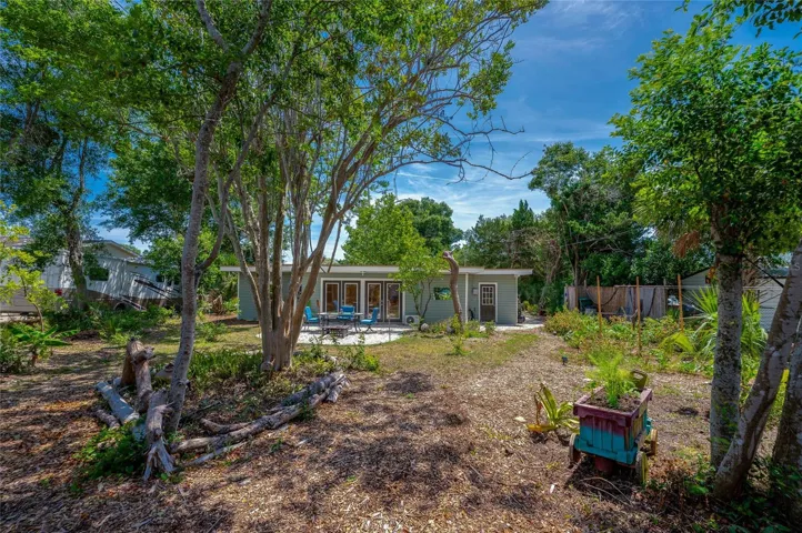 View from the spacious backyard looking back at the house, showing an intimate outdoor dining patio, mature shade trees, and a decorative garden planter.