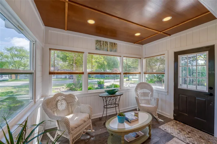Inviting front entryway and sunroom boasting a classic dark entry door alongside large windows that let in abundant natural light. Warm wood ceiling panels, and multi-colored floor tiles create an instantly welcoming atmosphere.