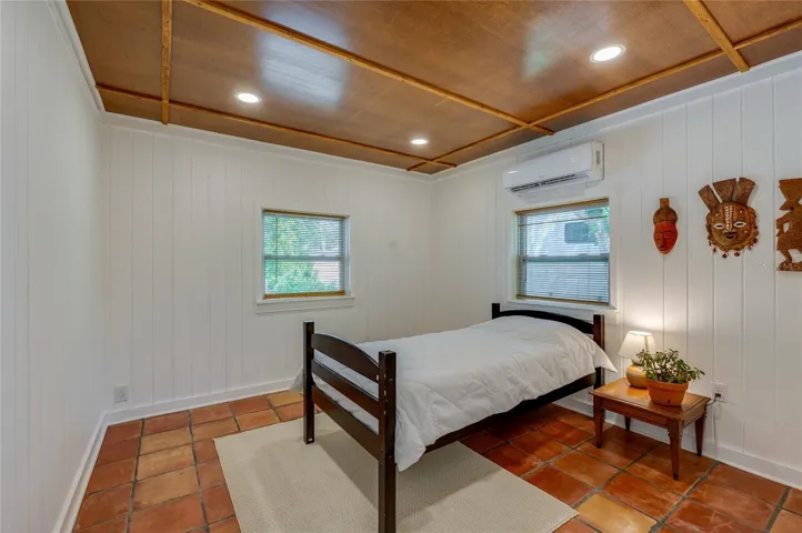 Cozy bedroom showcasing white paneled walls. The room is complete with a mini-split air conditioner, and tile flooring.