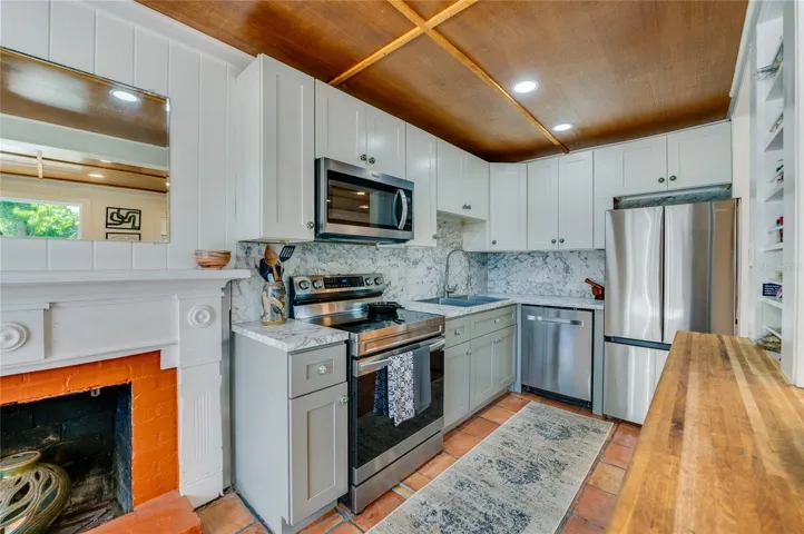 Detailed view of the functional kitchen workspace featuring a premium stainless steel range, built-in microwave, and a classic fireplace with a vibrant orange interior accent. Smart storage solutions include sage green cabinetry and an integrated spice rack shelf.