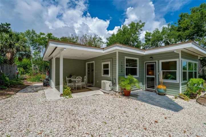 Close-up exterior of the modern sage-green home, highlighting the covered front porch, gravel entryway, and neat architectural lines.