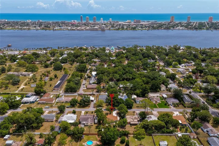A high-altitude aerial image showcases the neighborhood context, with a prominent red arrow identifying the property. The background features coastal high-rises and the ocean along the horizon.