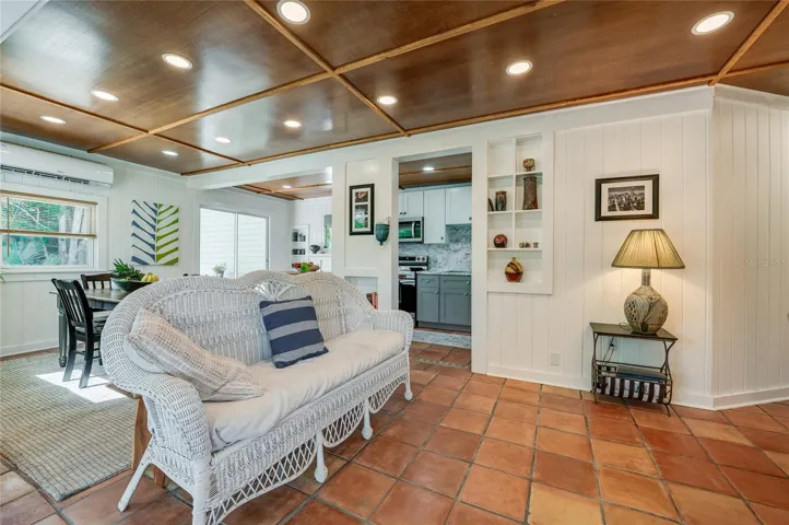 Spacious living area showcasing the elegant rustic floor tiles, and a rich wood-paneled ceiling with modern recessed lighting. The open-concept layout seamlessly transitions into the adjacent dining room and kitchen spaces.