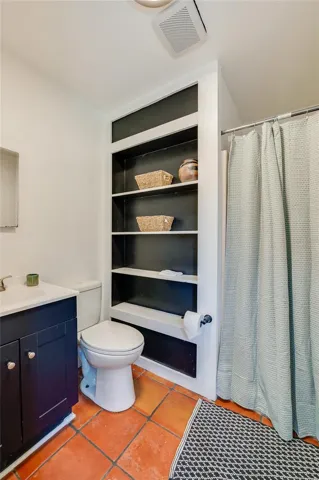 Full bathroom featuring a vanity, a white toilet, and unique built-in open shelving with a black backdrop for storage.