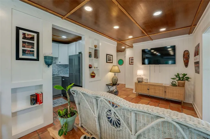 Comfortable media room highlights crisp white walls and warm tile floors. The view looks back toward an open doorway into the modern kitchen.