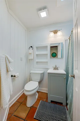 Bathroom maximizing efficiency with a grey vanity, a recessed wall shelf, and a clean white toilet. Floor tiles add character, paired with a modern light fixture above the mirror.