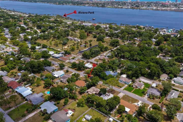 Looking back from a different angle, this aerial photo shows the home marked by a red arrow amidst mature trees. The other arrow pointing toward Riviera Park visible along the shoreline.