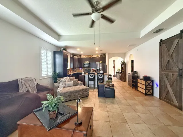 View of living room and kitchen and entry from the sliding glass doors of the covered and screened in lanai. Trey ceiling, ceramic tile flooring, plantation shutters, barn door leading into the primary bedroom.