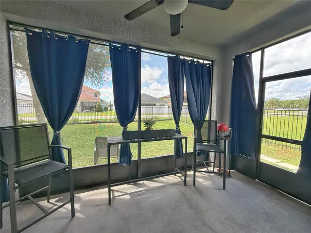 Covered and screened in lanai with curtains with view of fenced in backyard