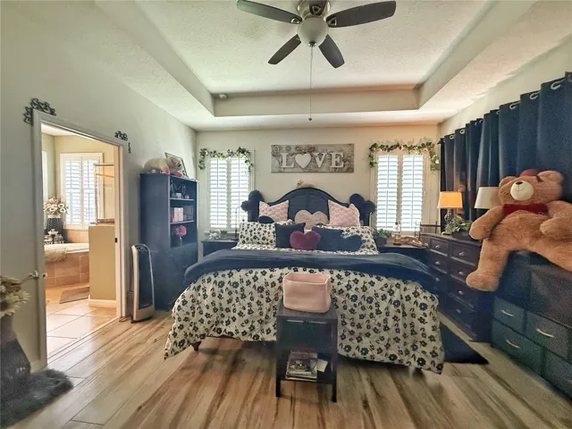Additional view of primary bedroom with Tray ceiling, laminate flooring, view of primary en suite bathroom, plantation, shutters, walk-in closet