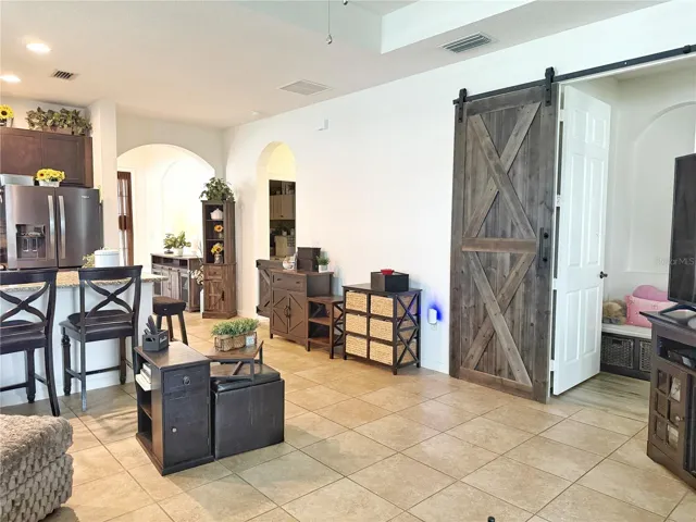 Closer view from living room of kitchen with bar top seating, half barn door leading into laundry room, bedrooms, two and three and guest bathroom, and large barn door leading into primary bedroom
