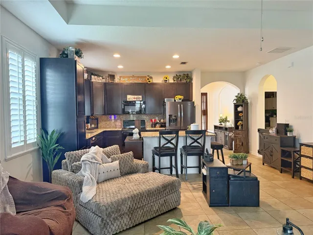 View from the living room of the kitchen, the entry and hallway into the laundry recess can lighting, 42 inch cabinets, backsplash, island with bar, top seating, plantation, shutters, tray ceiling in the living room