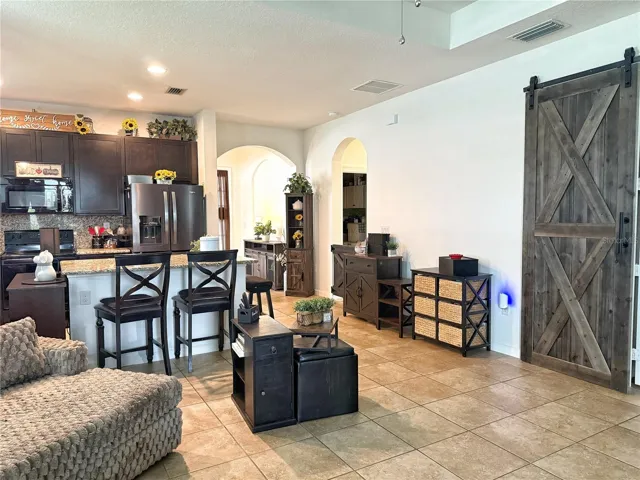 View from living room of kitchen, hallway to entry, laundry, room, and barn door that leads into the primary bedroom. Ceramic Tile Flooring, 42 inch cabinets with granite countertops, backsplash, island with bar, top seating