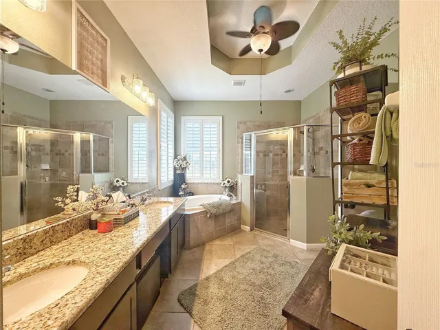 Primary bathroom with dual sinks, granite, countertops, garden tub, separate shower, tray, ceiling, ceramic tile, flooring, makeup space, private water, closet, and plantation shutters