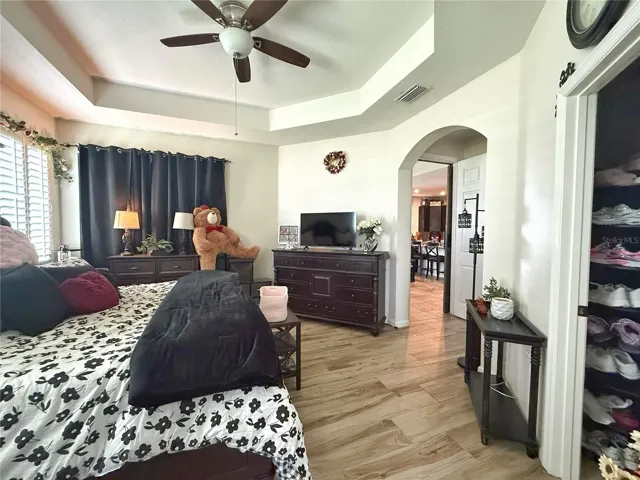 Primary bedroom with laminate flooring, tray, ceilings, plantation, shutters, sliding glass door leading onto the cupboard and screened in lanai, walk-in closet, en suite bathroom
