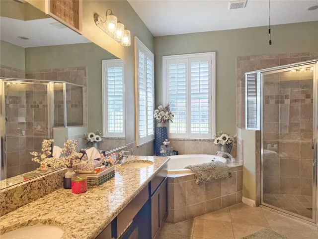 View of primary bathroom with plantation shutters, ceramic tile flooring, dual sinks with granite, countertops and vanity. Space, garden tub was separate shower and tray ceiling.