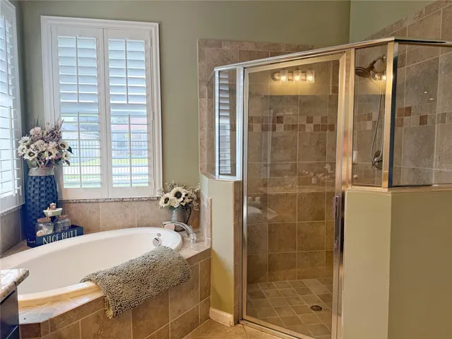Up close view of primary garden tub, and separate shower with plantation shutters