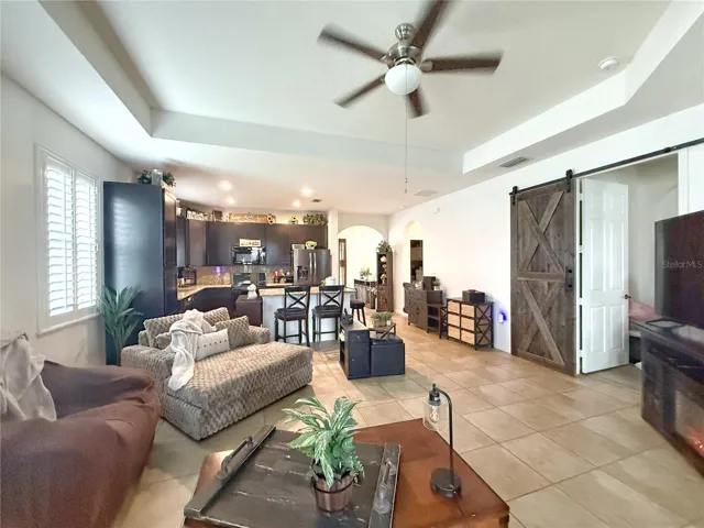 Living room with view of Kitchen with ceramic tile flooring, tray ceiling, plantation shutters, recessed can lighting