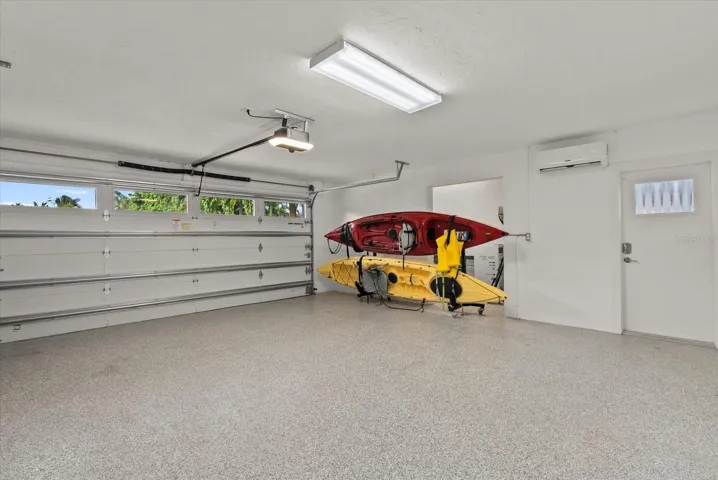 Large 2 car garage with mini-split AC, hurricane rated garage door installed in 2023, epoxy floor coating and separate storage room  (behind kayaks in this pic)