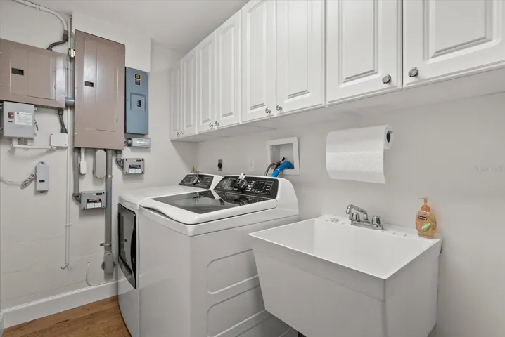 Indoor laundry room with new washer/dryer, upper storage cabinets, wash tub and closet.  Full electrical upgrade in 2024 with new panel, copper feeds and surge protection, including whole house generator (elevated).
