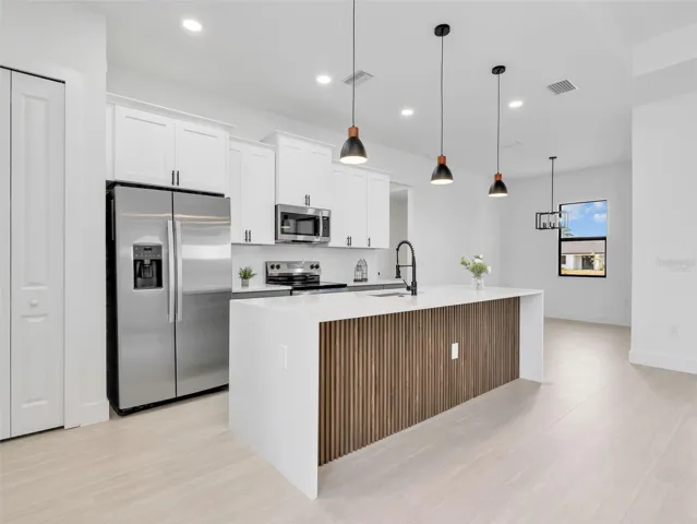 Contemporary kitchen featuring a waterfall island with a slatted wood-finish accent panel, quartz countertops, and stainless steel appliances