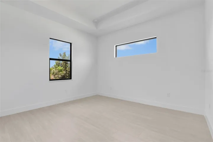 Primary Bedroom Bright interior space featuring light wood-finish flooring, white baseboards, and clean white walls and tray ceiling