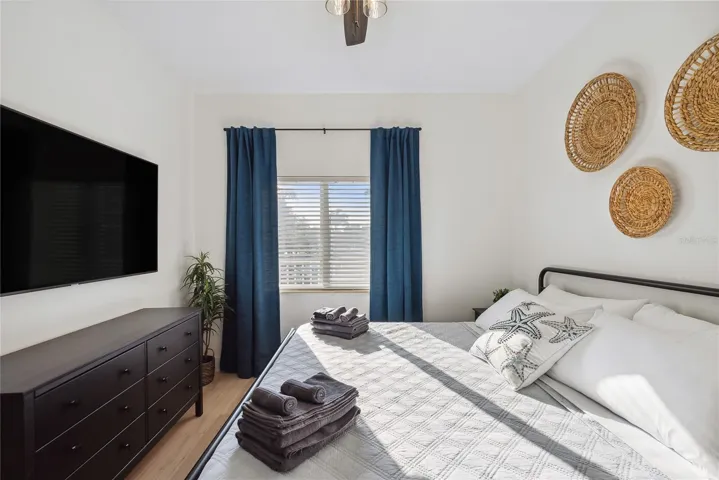Bedroom with ceiling fan, King bed, mounted smart TV, dresser, drapes and decor included