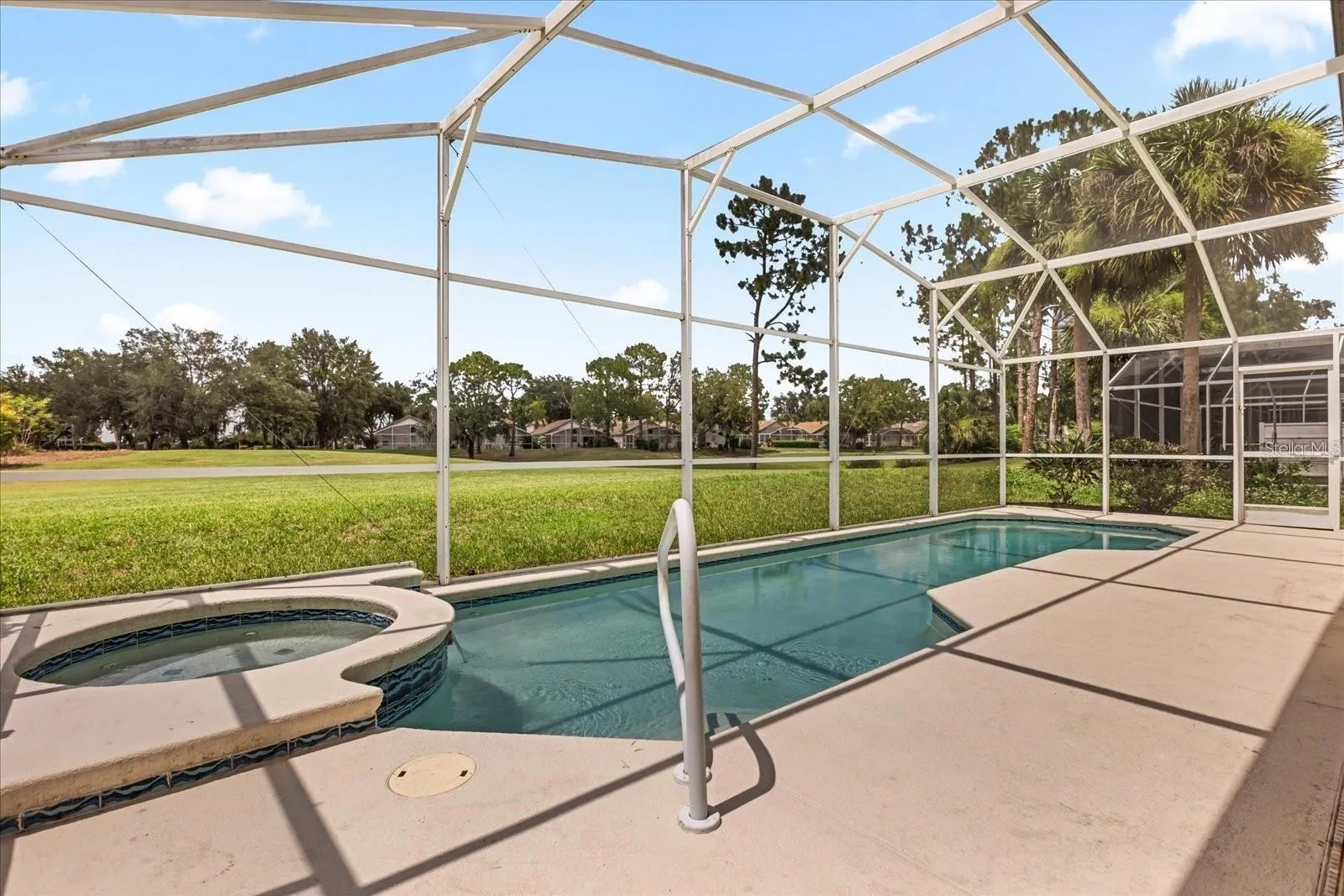 Sparkling pool and spa with screened enclosure and green space views