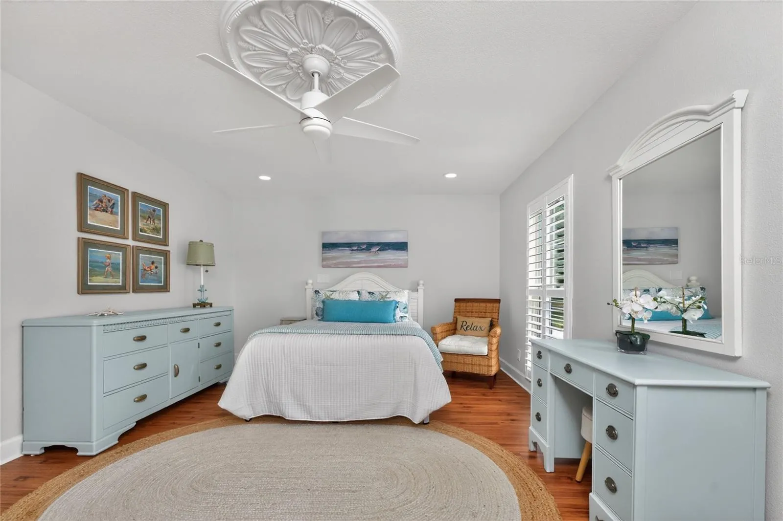 The spacious second bedroom features warm wood flooring plantation shutters, and a beautiful decorative ceiling medallion