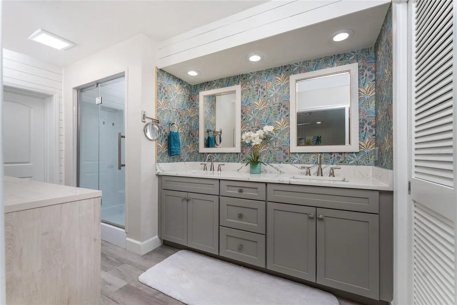The luxurious primary bathroom features an updated double vanity quartz countertop, a modern glass enclosed shower and a vibrant accent wallpaper.