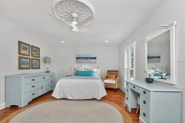 The spacious second bedroom features warm wood flooring plantation shutters, and a beautiful decorative ceiling medallion