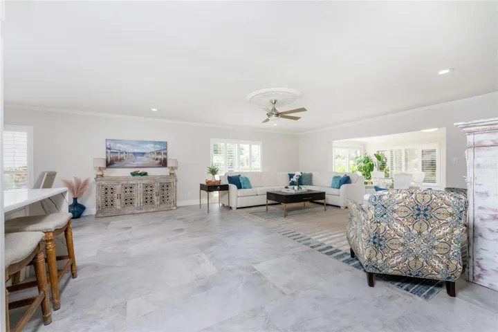 An expansive light living room boast a seamless open layout, A modern ceiling fan and elegant tile flooring throughout.