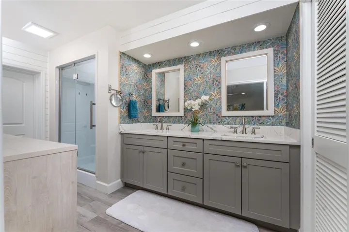 The luxurious primary bathroom features an updated double vanity quartz countertop, a modern glass enclosed shower and a vibrant accent wallpaper.