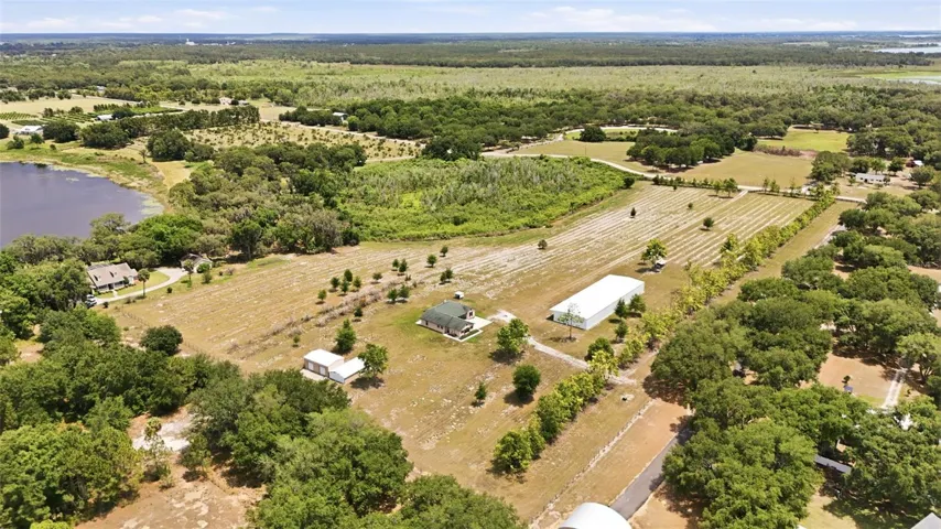 This sprawling aerial view captures the true scale and versatility of the property, showcasing the home, towering pines, open acreage, commercial-grade building, and endless room to live, work, store, and explore... all in one breathtaking setting.