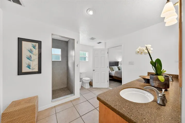 Private en-suite bath adjoining the second primary suite, offering excellent flexibility for guests, extended family, or in-law quarters. This spacious bathroom features a long vanity with generous counter space, warm cabinetry, and a tiled walk-in shower, creating a comfortable and functional retreat within the home.
