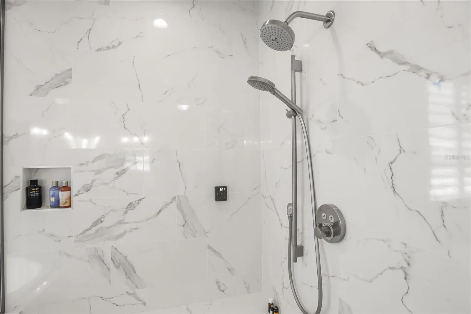 The oversized shower showcases marble-look tile, built-in niches, a bench, and multiple shower fixtures for an upgraded bathing experience.