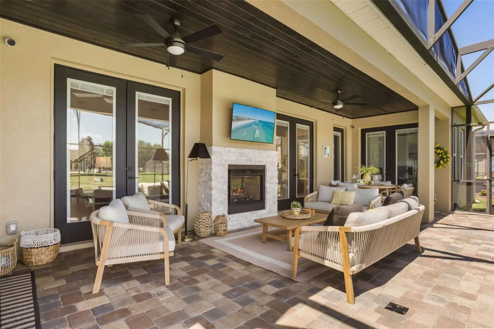 The covered lanai includes an outdoor fireplace, wall-mounted TV, ceiling fans, and multiple seating areas for year-round enjoyment.