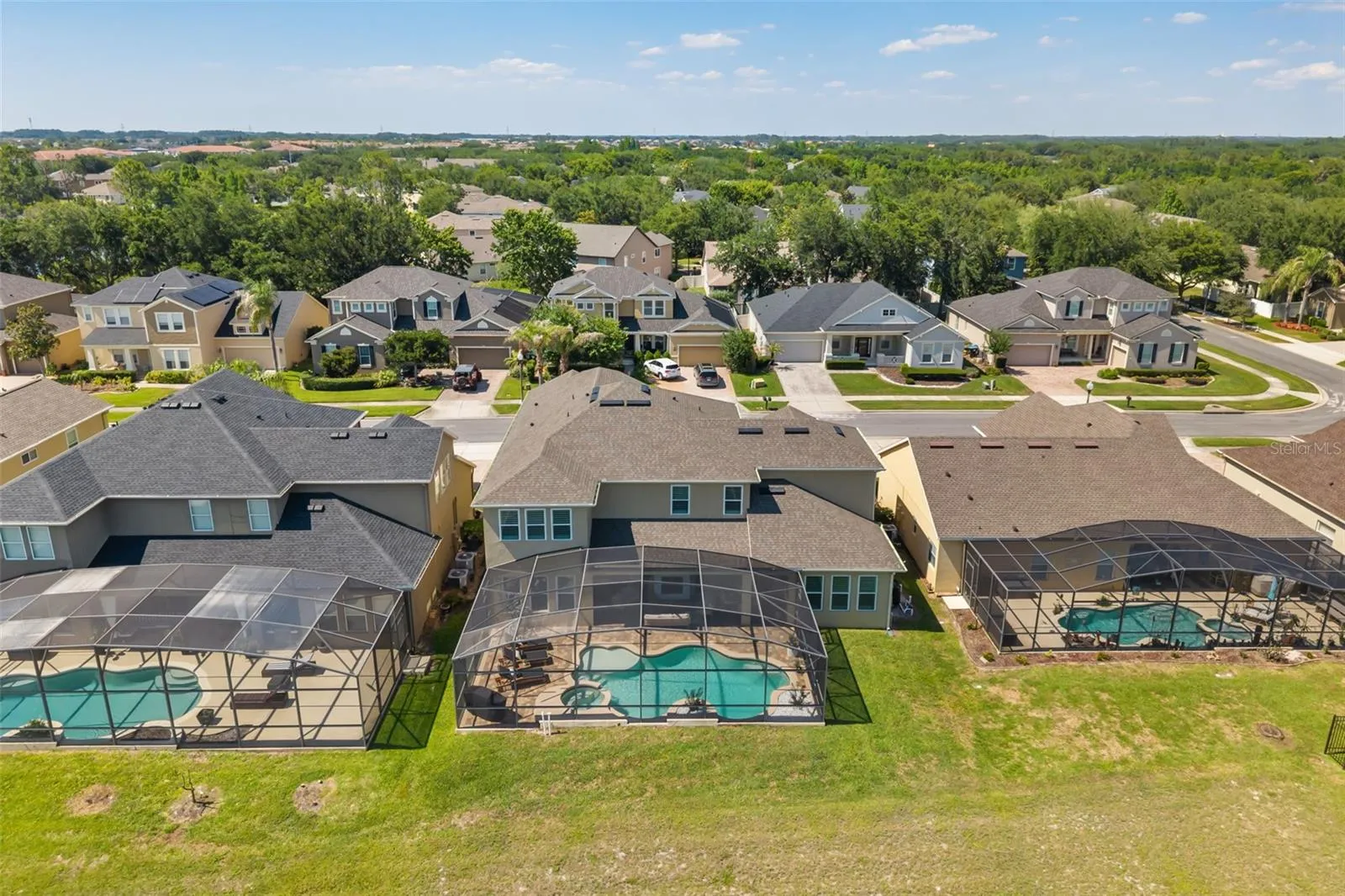 The elevated rear view shows the home’s pool enclosure, nearby green space, and established neighborhood surroundings.