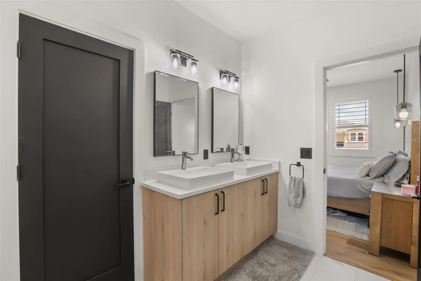 This ensuite bath includes a double vanity with vessel sinks, wood-tone cabinetry, black hardware, and modern lighting.