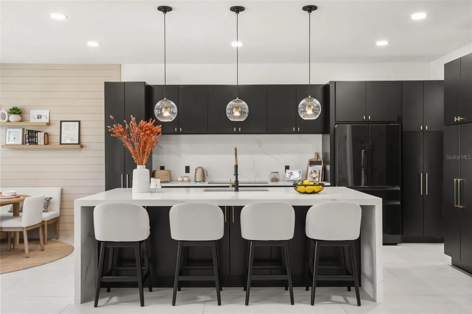 Sleek black cabinetry, brass hardware, and a full-height marble-look backsplash create a bold, contemporary kitchen design.